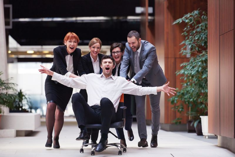 Group of people in office pushing man on chair laughing