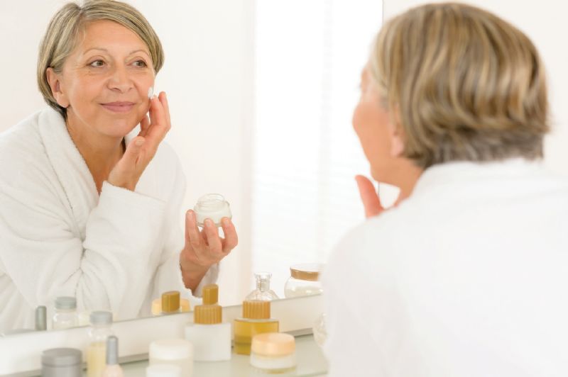 Senior woman putting on face cream mirror bathroom