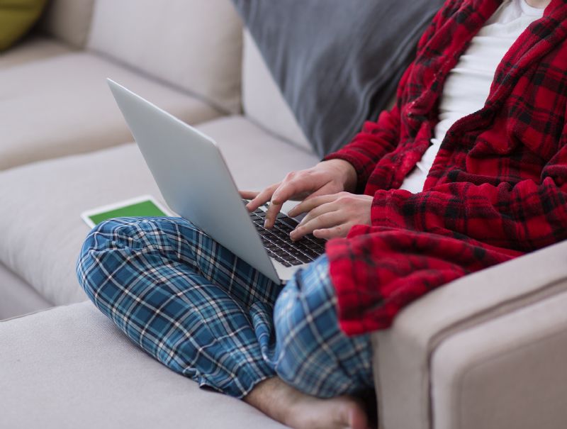 Man sat on sofa in pyjamas typing on laptop