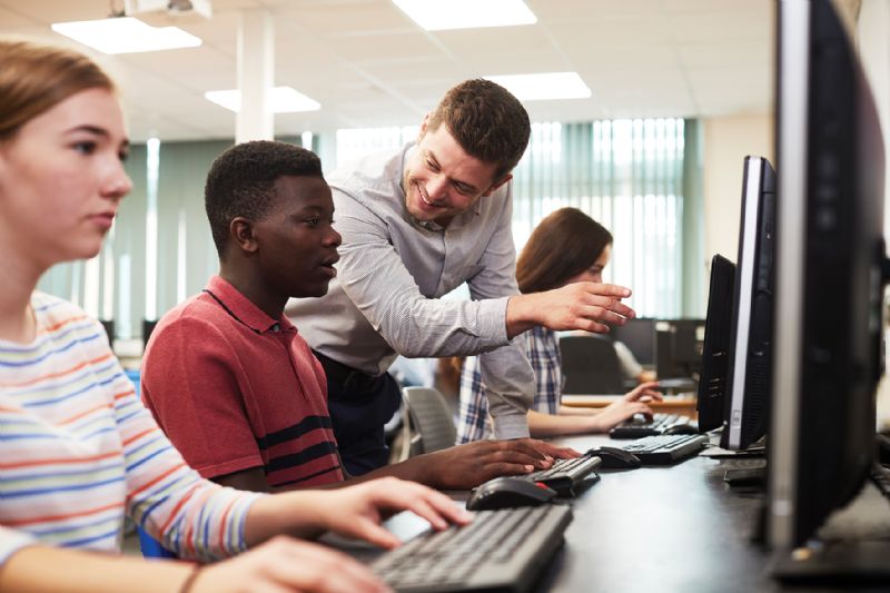 Young male student talking with teacher computer lesson